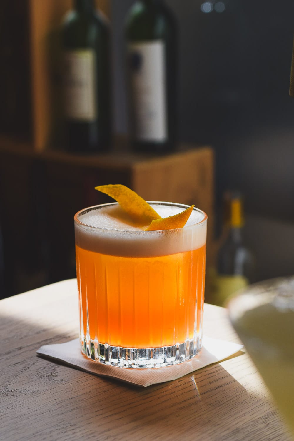 Sour-cocktail med skum og appelsinskal i sollys.